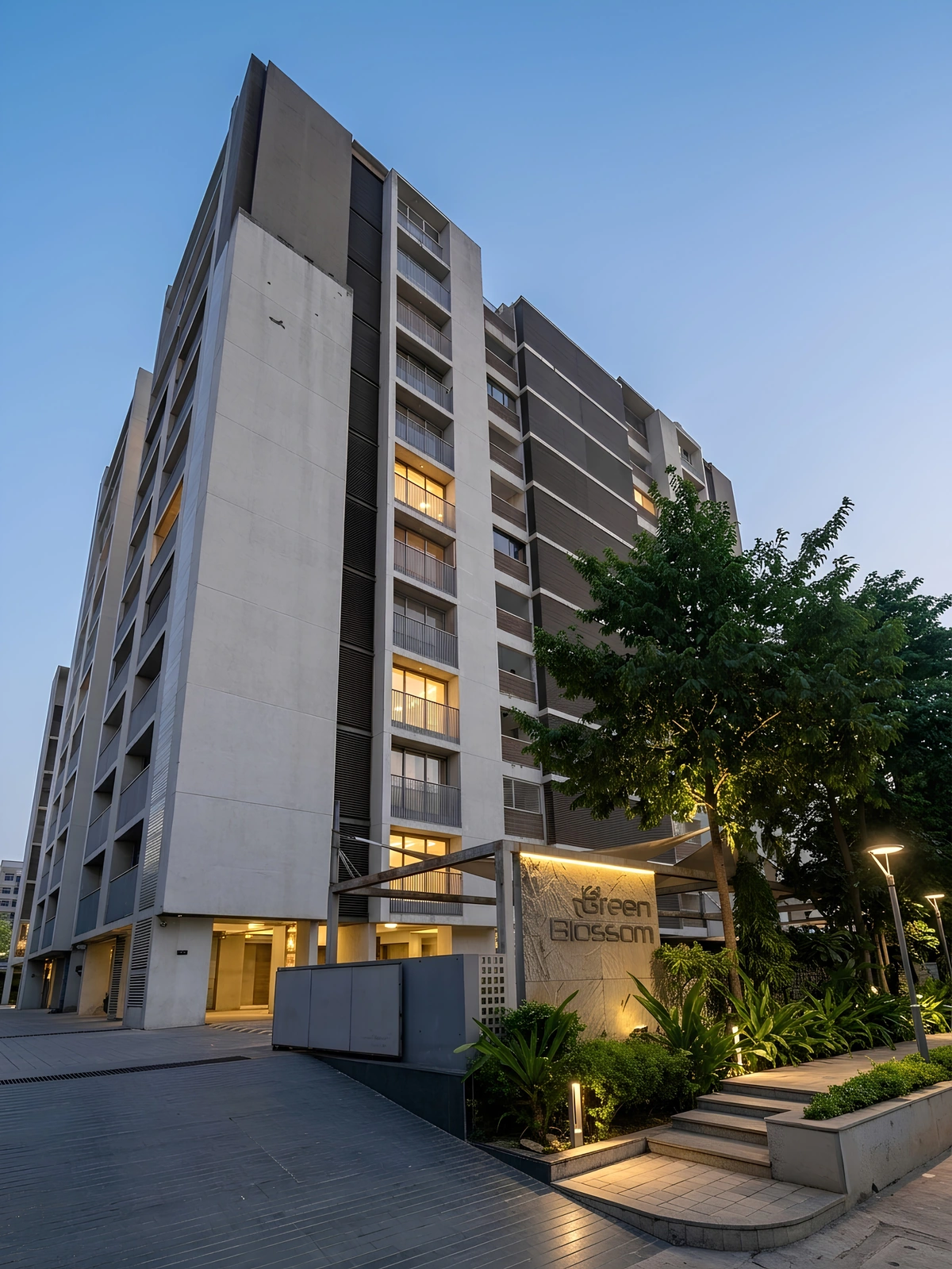 Green Blossom's residential tower at dusk, with its landscaped entrance and illuminated name sign.
